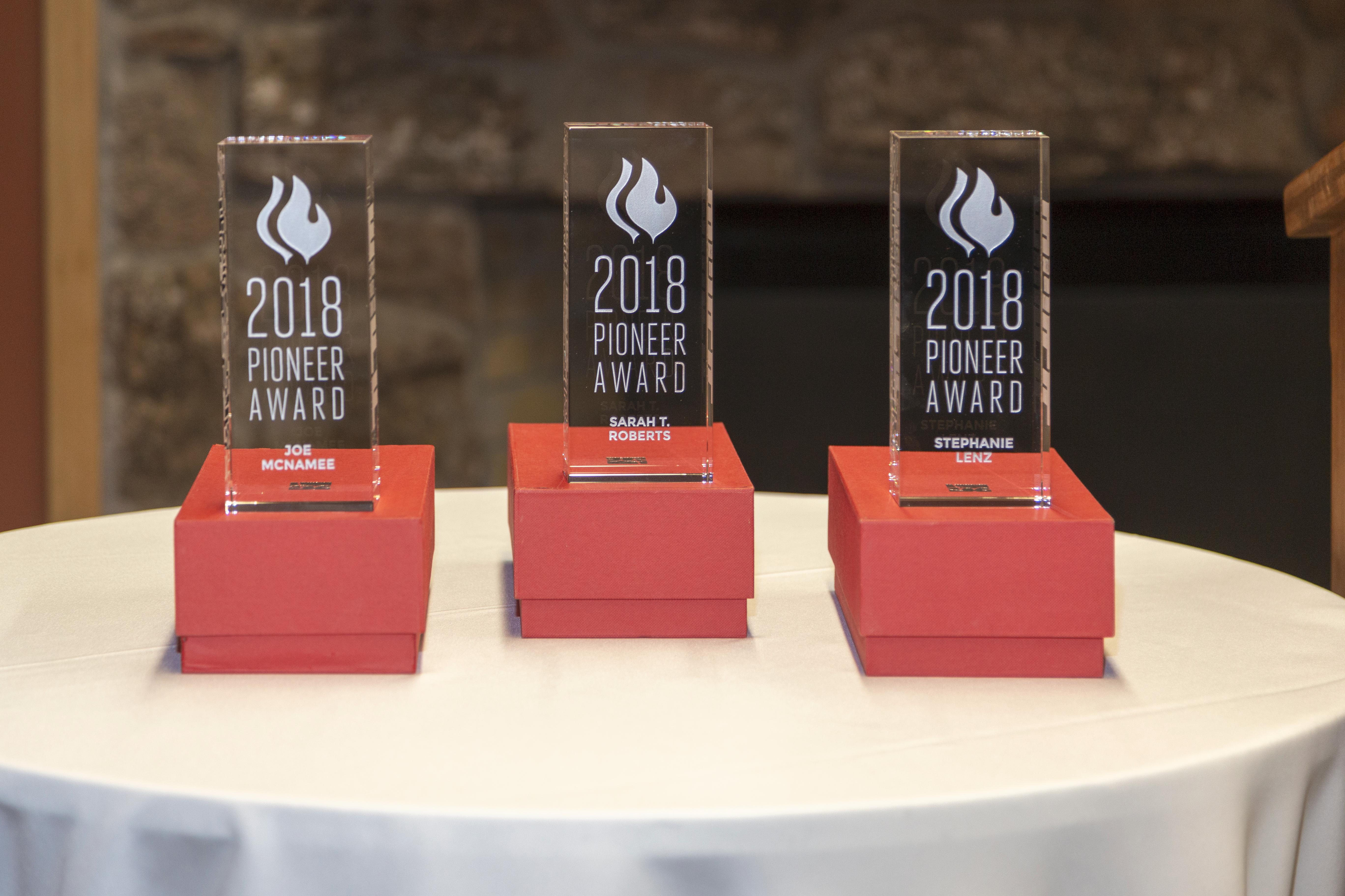 Three 9" by 3" by 2" rectangular awards in clear acrylic. Front engraved with "2018 Pioneer Award" and "Joe McNamee", "Sarah T. Roberts" and "Stephanie Lenz", respectively.