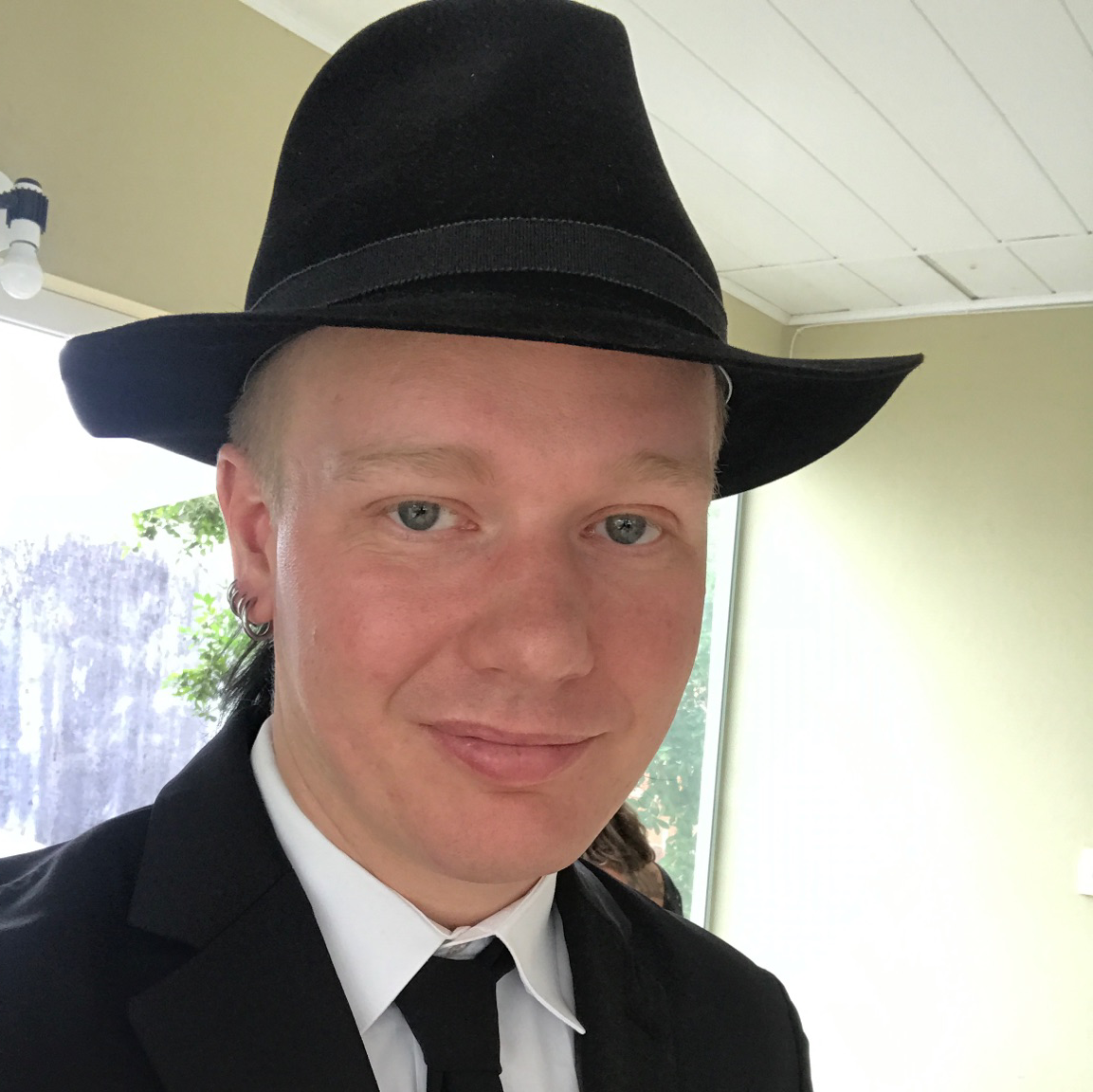 A picture of ola bini. The picture shows a young man in a suit and tie, wearing a black hat.