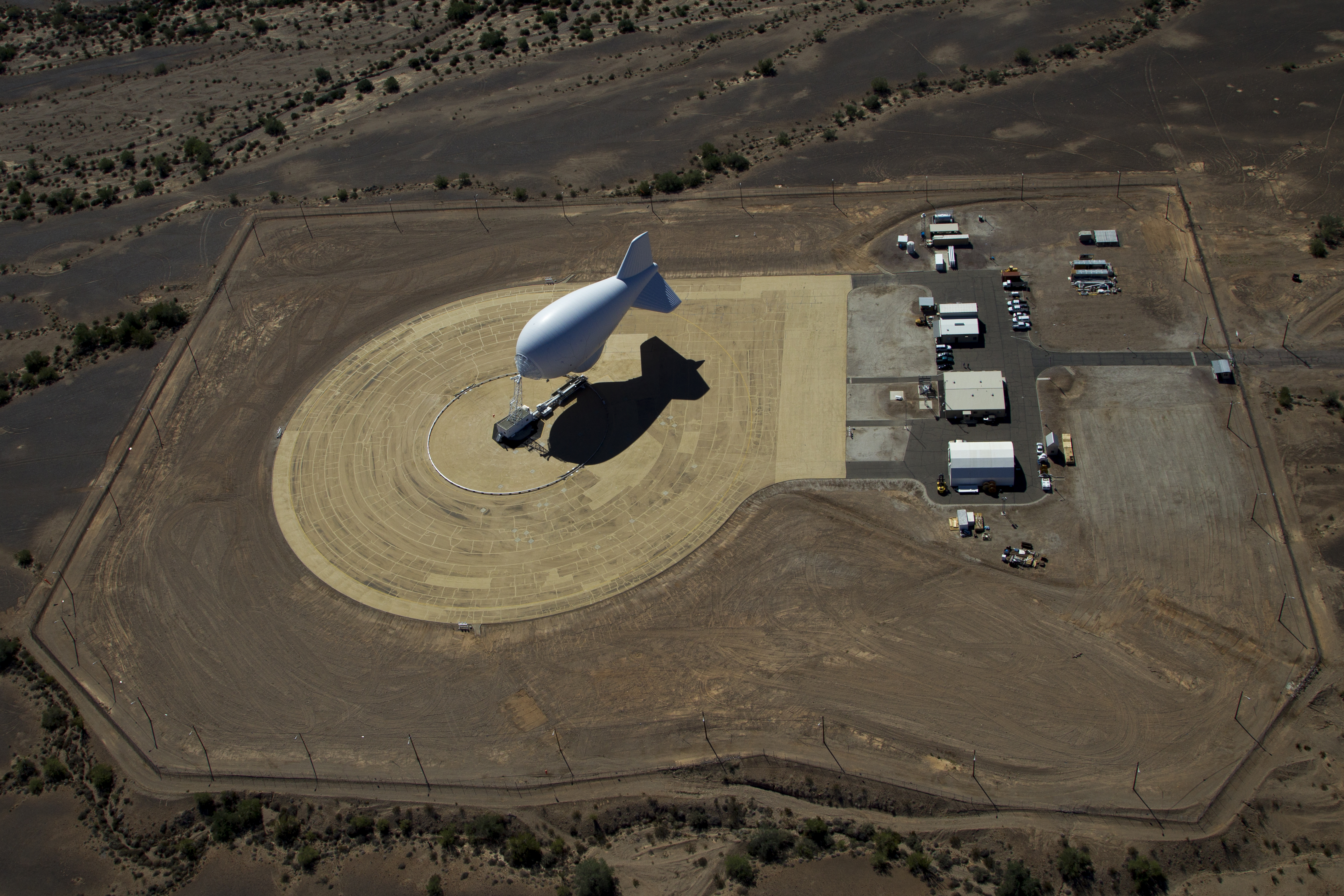 A blimp-shaped surveillance balloon is moored in an open space.