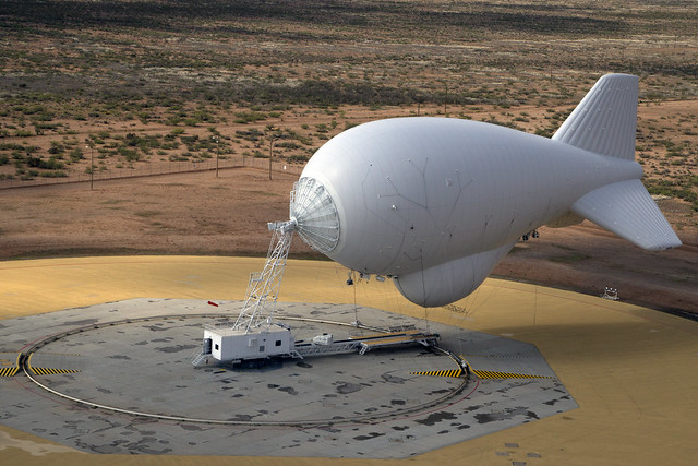 A white blimp floats above the desert