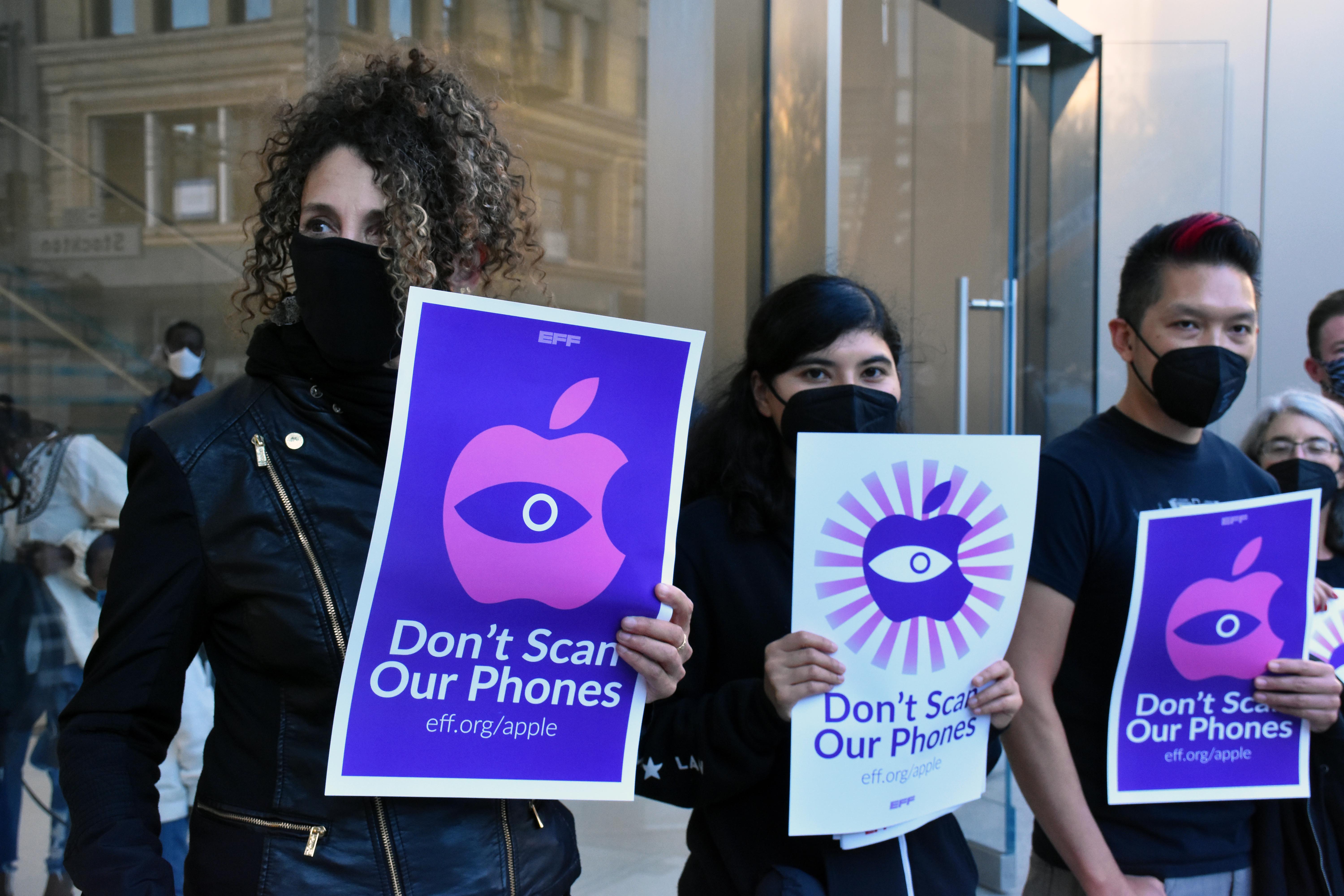 three people holding signs stand in front of apple store