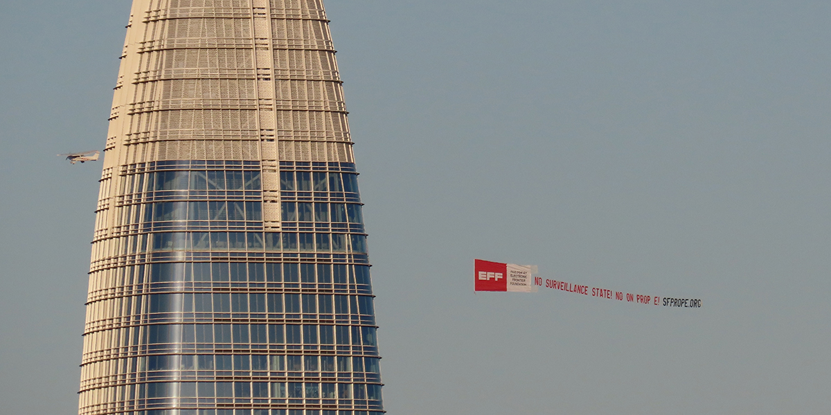 A plane flying over san francsico skyline carrying a banner asking people to vote no on Prop E