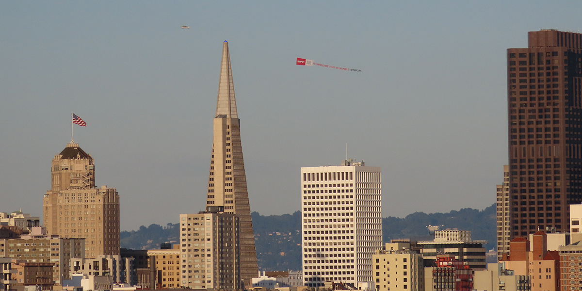 A plane flying over san francsico skyline carrying a banner asking people to vote no on Prop E