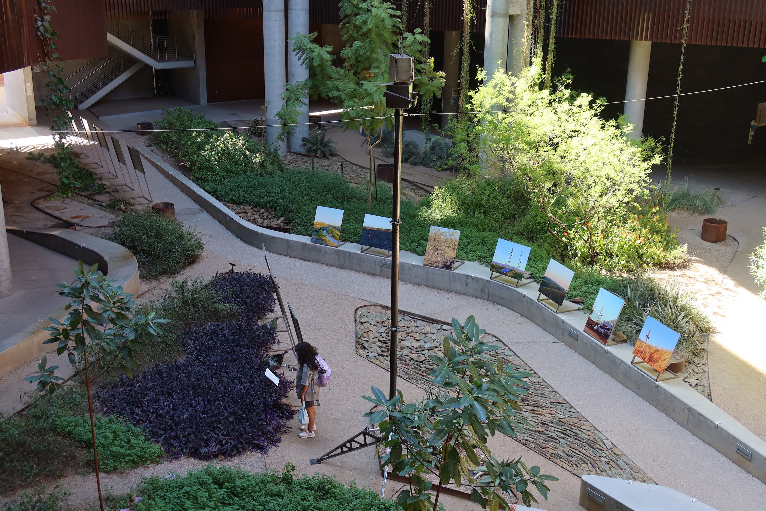 An overhead view of a University of Arizona courtyard with a model surveillance tower and mounted photographs of surveillance technology. A person looks at one of the displays.